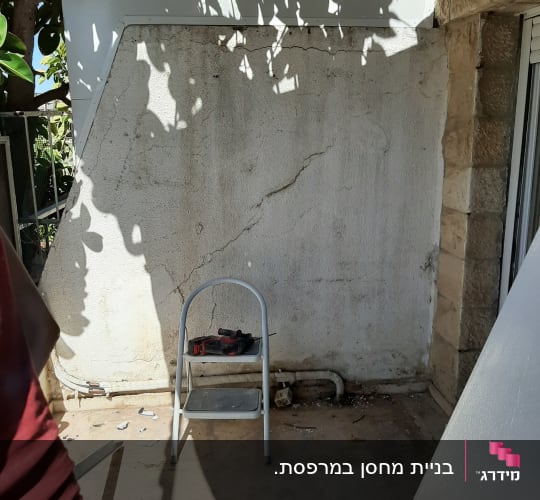 קיר עם סדקים, סולם קטן וכלי עבודה על הרצפה
